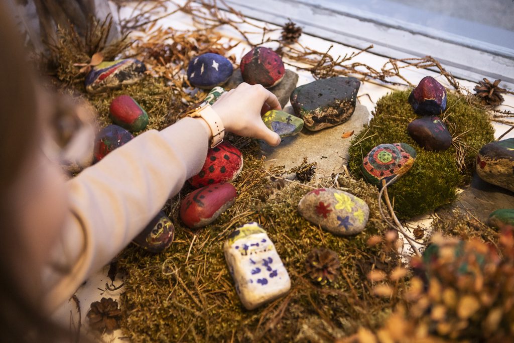 Henkilö asettaa maalattua kiveä muiden kivien ja luonnonmateriaalien joukkoon.